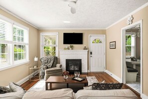 A living room with a fireplace, a television, and a door leading to a bathroom. - Blue Door Cottage: Downtown charm & convenience, dog-friendly large fenced yard (Aiken)
