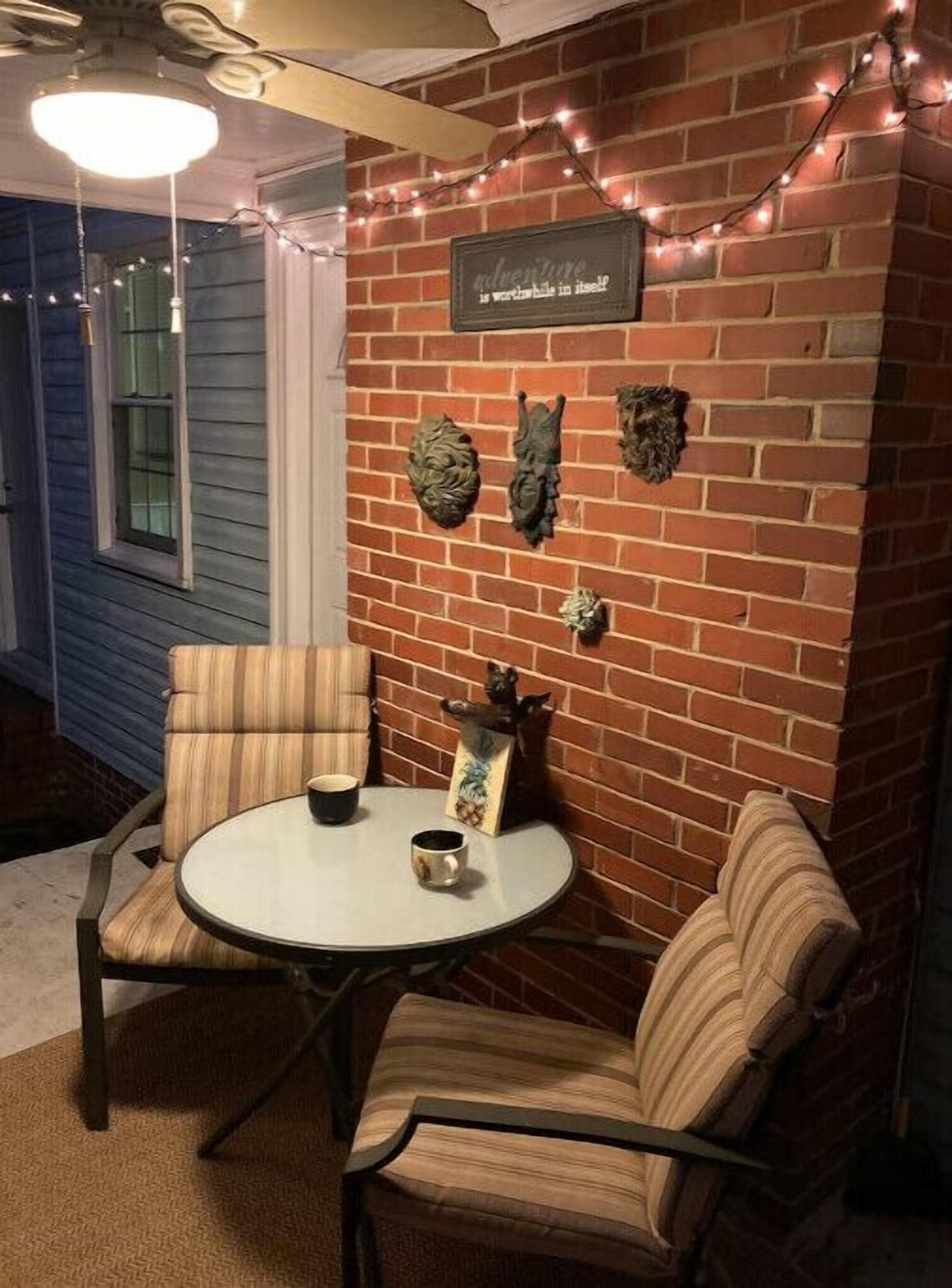 A cozy outdoor seating area with a brick wall, string lights, and decorative wall art.