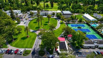 An aerial view of a golf course with a tennis court, parking area, and surrounding greenery.