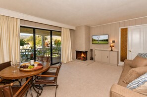 A living room with a fireplace, a television, a dining area with a table set for a meal, and a view of the outdoors.