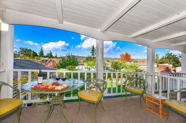 A covered outdoor area with a glass table set for dining, surrounded by chairs.