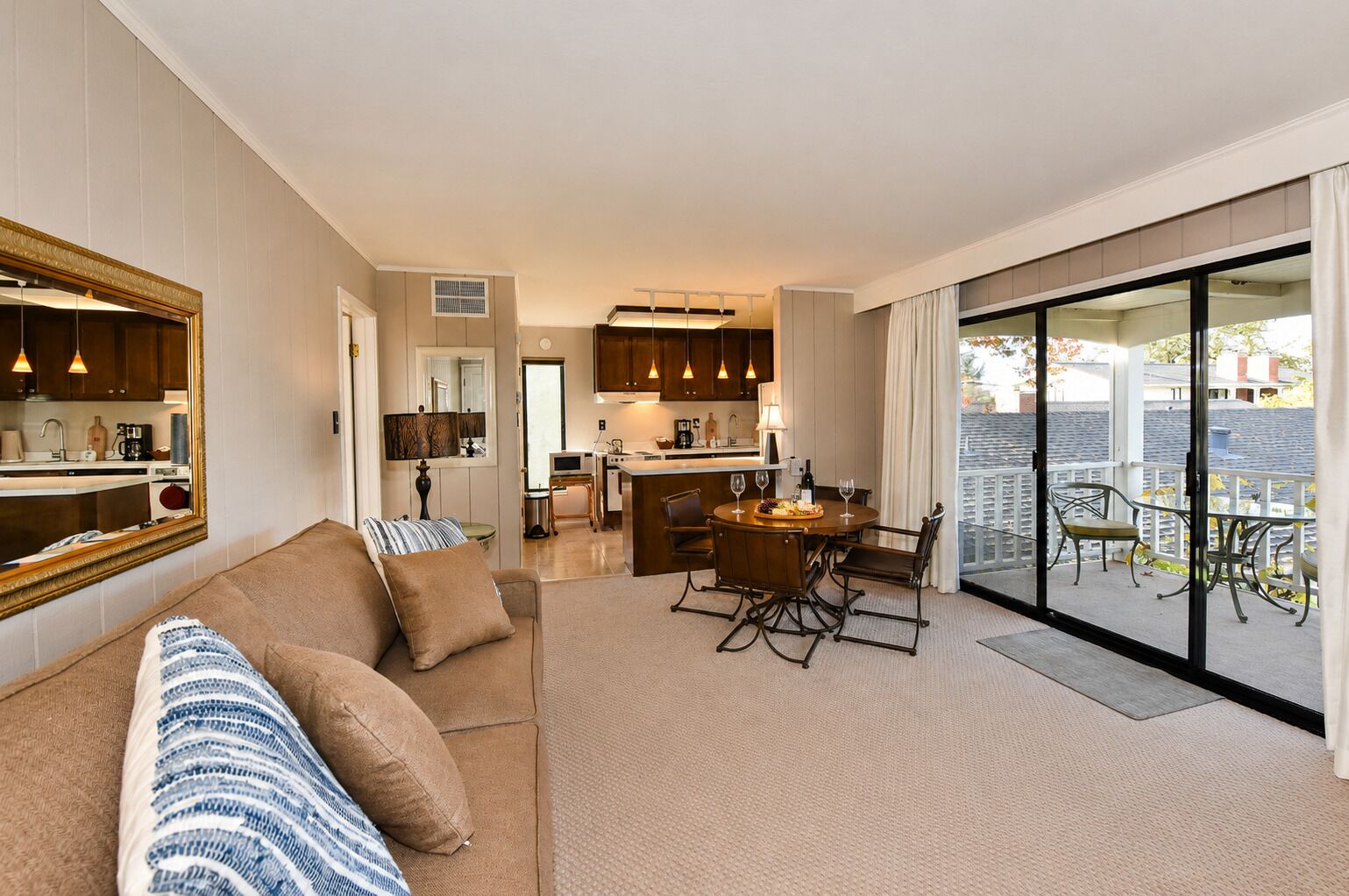 A modern living room with a sofa, a dining area with a table and chairs, a kitchen with cabinets, and a balcony with outdoor furniture.