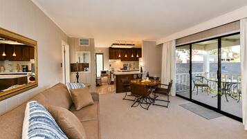 A modern living room with a sofa, a dining area with a table and chairs, a kitchen with cabinets, and a balcony with outdoor furniture.