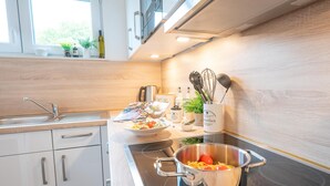 A modern kitchen with white cabinets, a stove, and a pot on the counter. - Ferienhaus Marschengrün Büsum (Büsum)