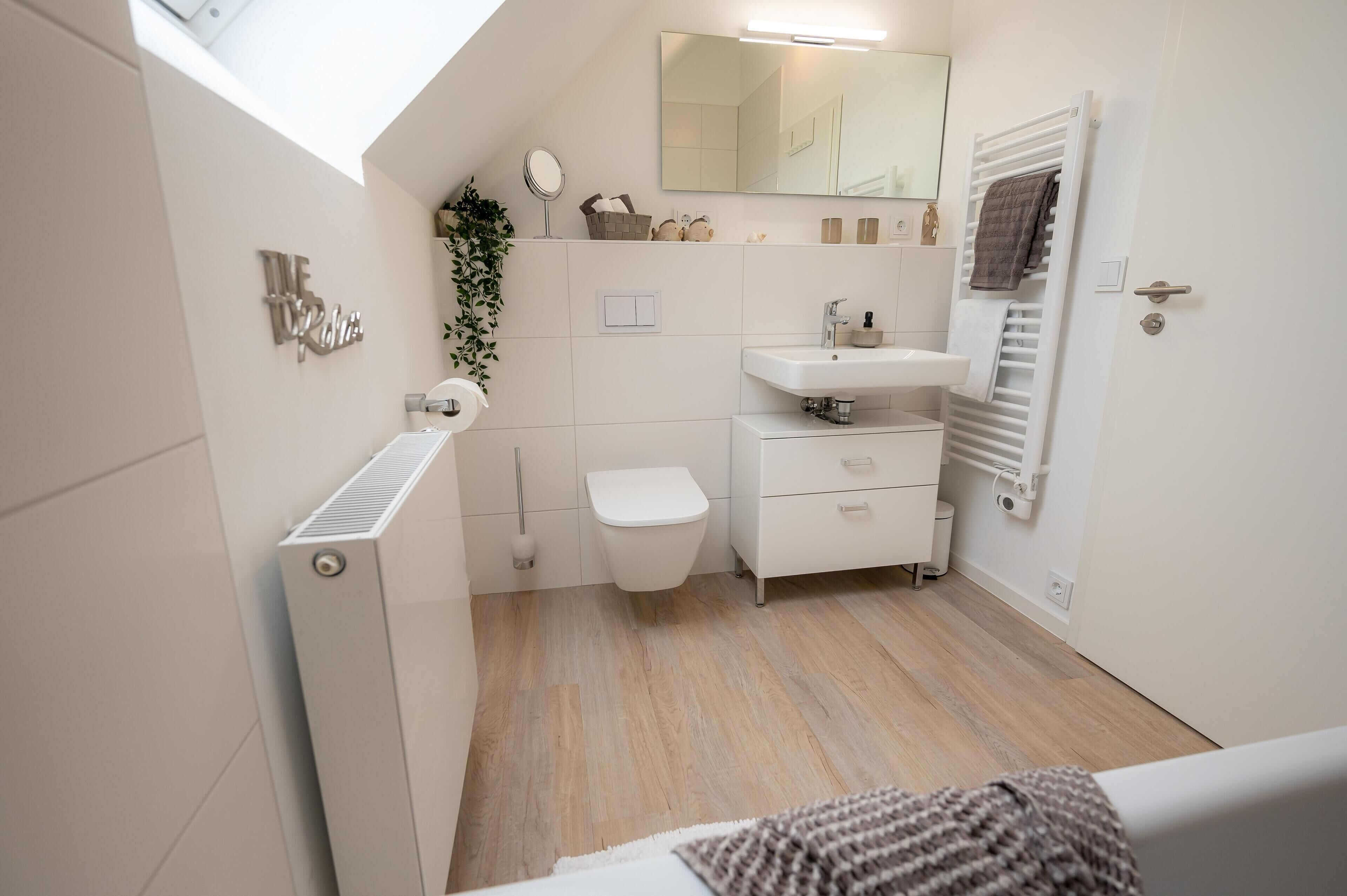Un baño moderno con tragaluz, sanitarios blancos, radiador y barra para toallas.