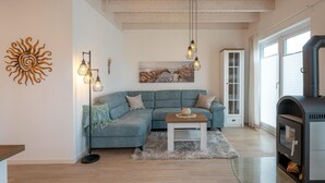 A modern living room with a sectional sofa, a glass coffee table, a fireplace, and a large window. - Ferienhaus Marschengrün Büsum (Büsum)