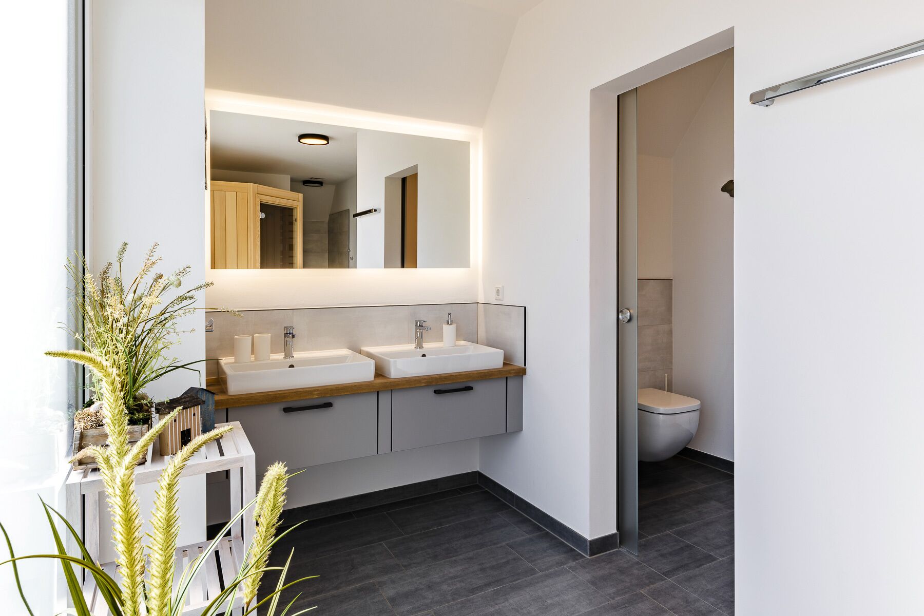 Une salle de bain moderne avec deux lavabos, un grand miroir et des toilettes.