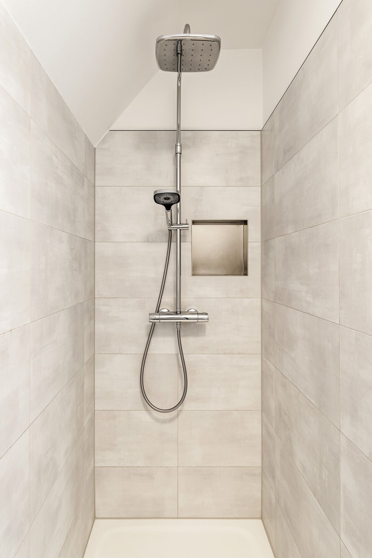 Une douche moderne dotée d’un pommeau de douche à main et d’un pommeau de douche fixe, le tout fixé sur un mur avec un panneau rectangulaire.