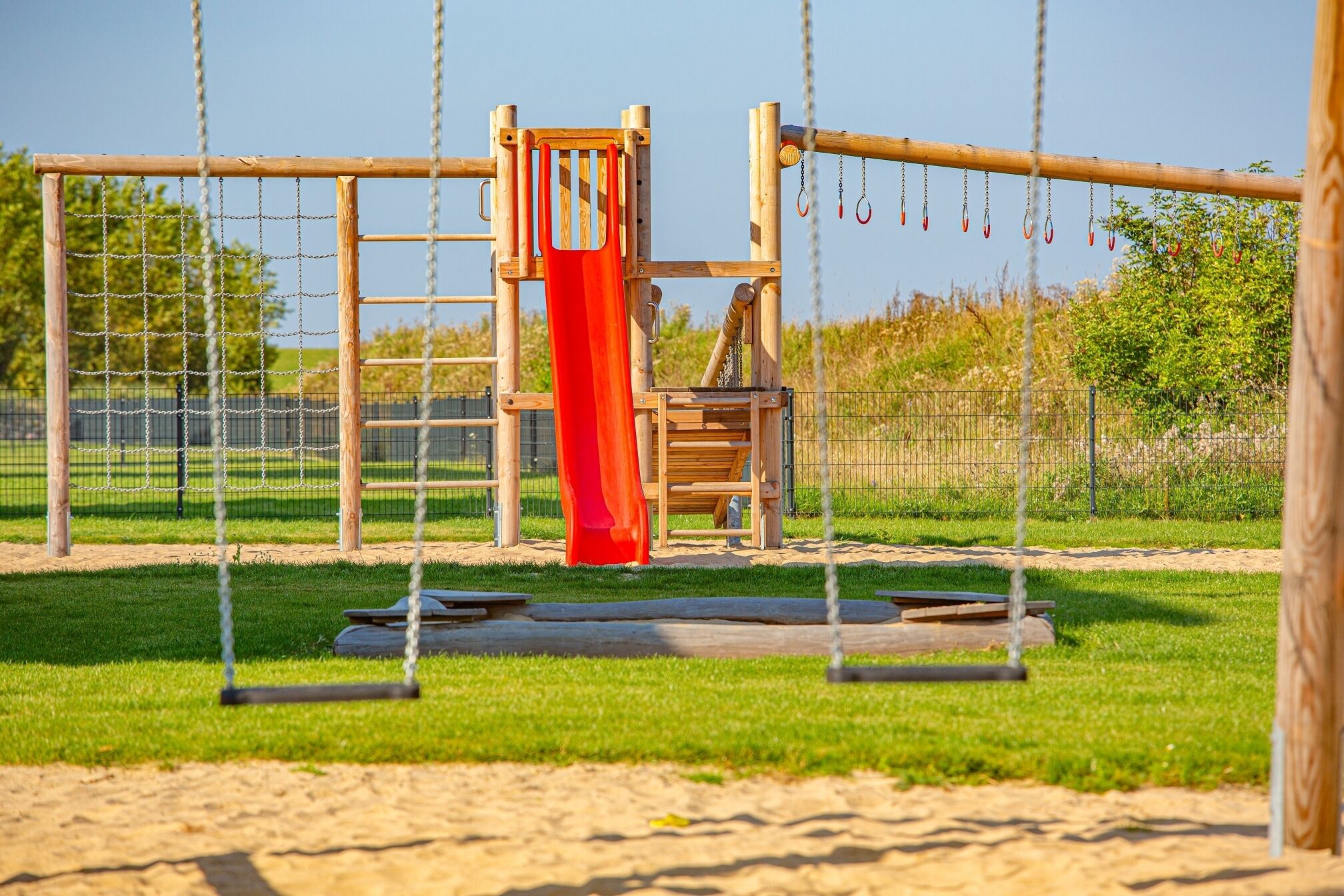 Ein Spielplatz mit Rutsche, Schaukeln und einer Kletterkonstruktion.