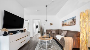 Un salon moderne avec un téléviseur à écran plat, un meuble de rangement blanc, un canapé marron et une table basse ronde.