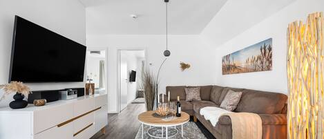 A modern living room with a flat-screen TV, a white entertainment unit, a brown sofa, and a round coffee table.