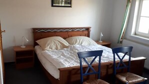 Una camera da letto con un letto in legno, due comodini, una scrivania, due sedie blu e una finestra.