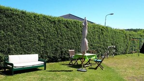 Spazio esterno curato con prato verde, divano bianco, tavolo con tovaglia verde e altalena.
