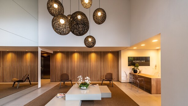 A modern reception area with a wooden panel wall, a reception desk, and a seating area with a white coffee table and chairs. - Pinheiros Best Studio Pool Parking  Wifi (São Paulo)