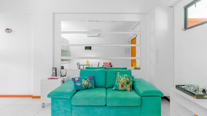 A modern living room with a teal sofa, white walls, and a built-in shelving unit. - RV09 Apto Vista Mar - Rio Vermelho (Salvador)