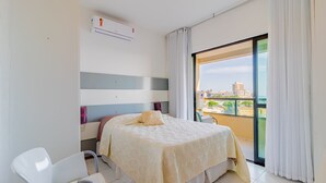 A hotel room with a bed, a chair, a balcony with a city view, and an air conditioning unit. - RV09 Apto Vista Mar - Rio Vermelho (Salvador)