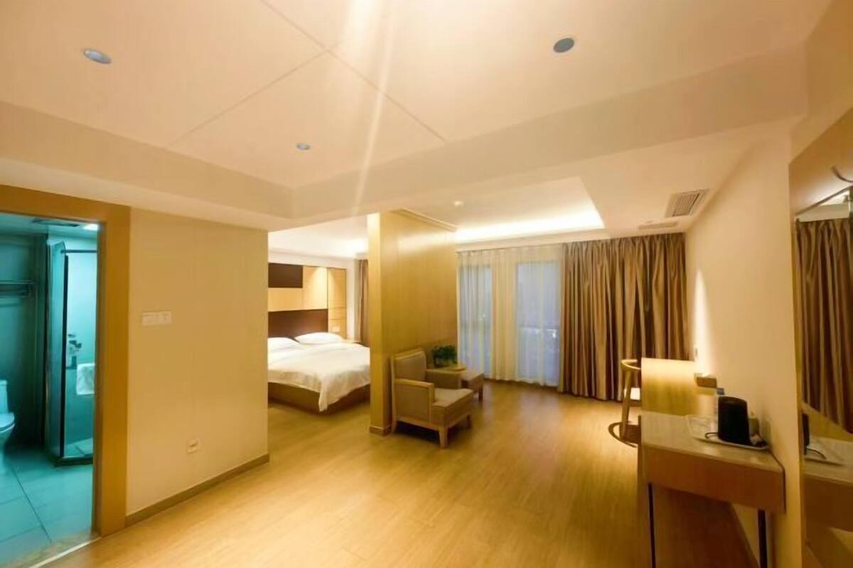A hotel room with a bed, a chair, a desk, and a bathroom visible through an open door.