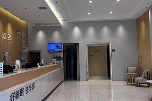Zona de recepció d'hotel amb una taquilla, una pantalla de televisió i un passadís que condueix a altres habitacions.
