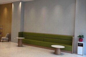 Una zona de recepció amb un sofà verd, dues taules rodones i una planta petita en test.