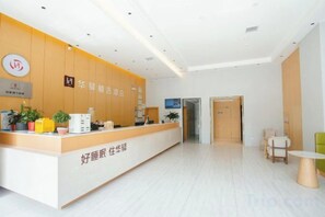 A hotel reception area with a reception desk, a plant, and a seating area with a table and chairs. - Home Inn UP Huayi Collection (Lu'an Railway Station Branch) (Lu'an)