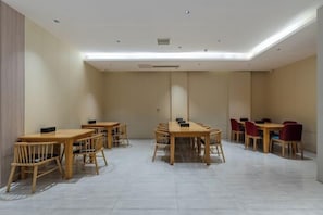 Een vergaderzaal met meerdere tafels en stoelen, een betegelde vloer en inbouw plafondverlichting.