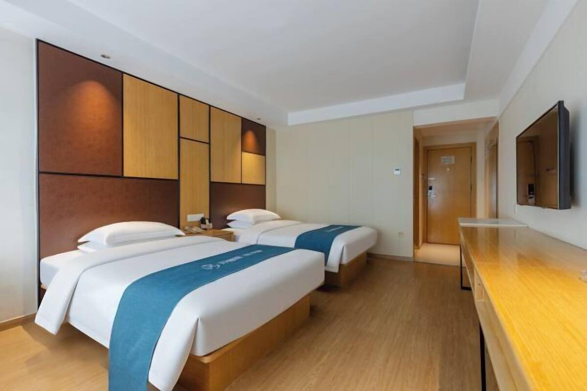 A hotel room with two beds, a wooden floor, a flat-screen TV mounted on the wall, and a door leading to another room.