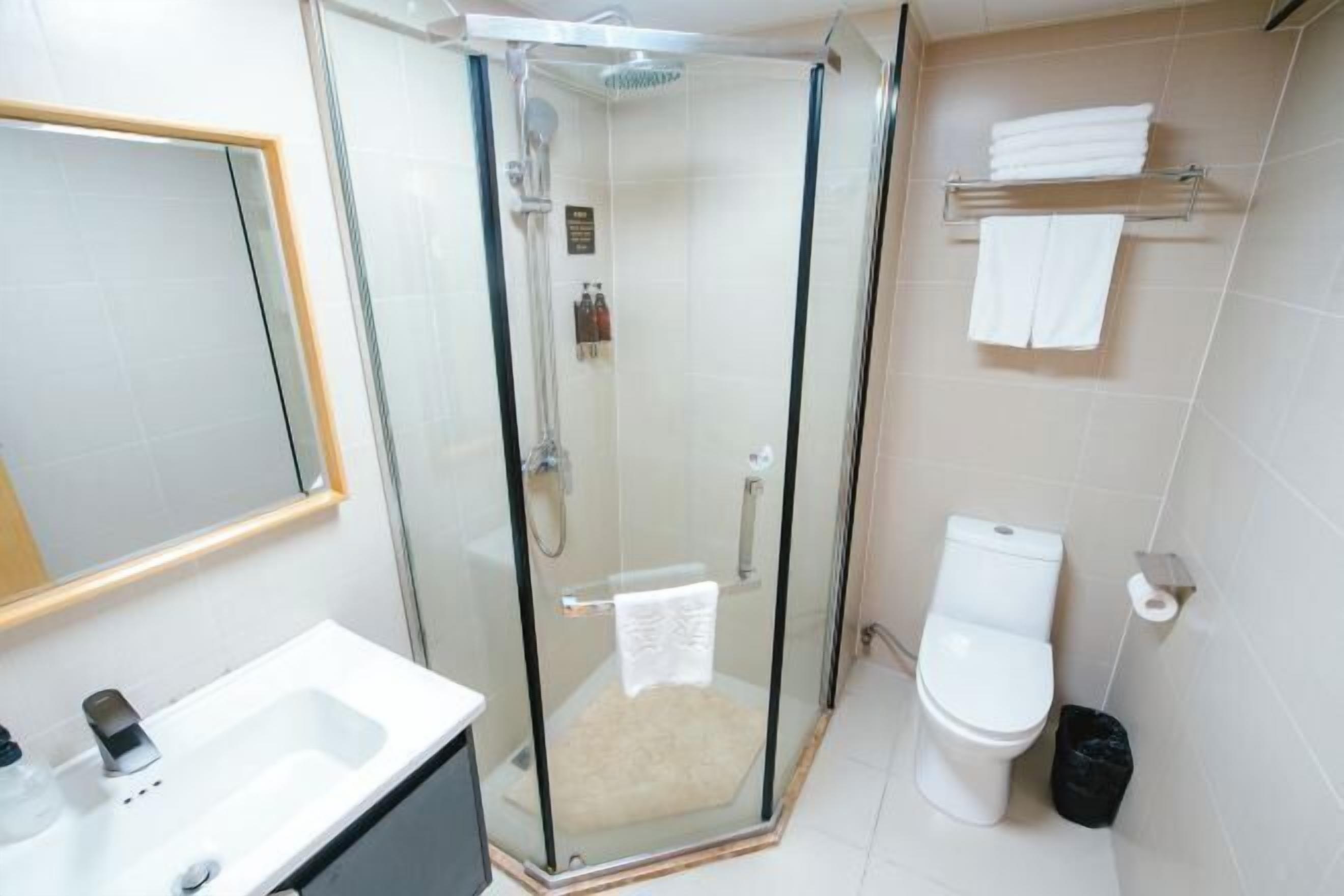 Un baño moderno con ducha de vidrio, lavamanos blanco, inodoro y toallero.