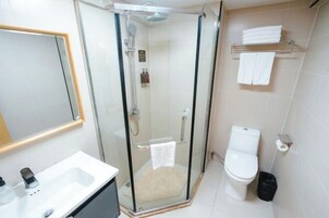 Un baño moderno con ducha de vidrio, lavamanos blanco, inodoro y toallero.