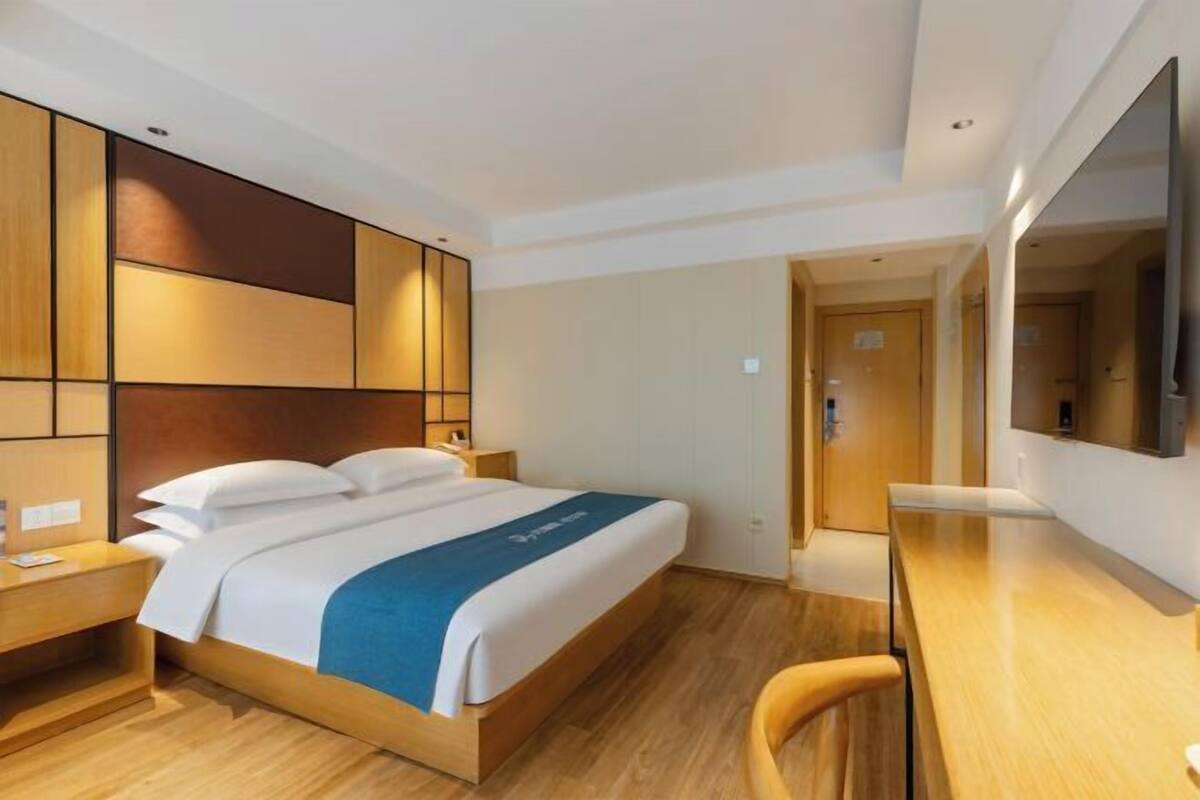 A hotel room with a bed, bedside table, desk, chair, and a TV mounted on the wall.