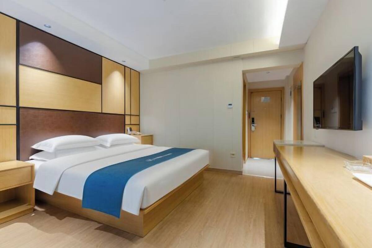 A hotel room with a bed, bedside table, TV, and a wooden desk.