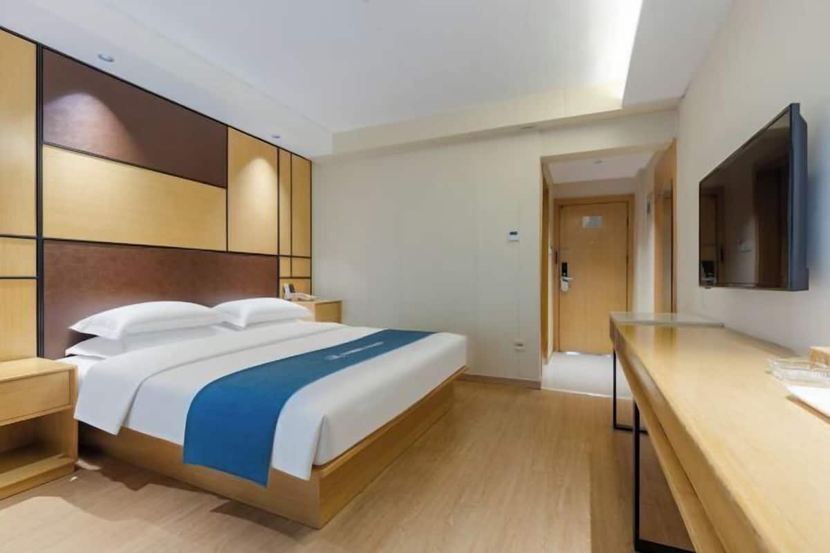 A hotel room with a bed, bedside table, TV, and a wooden desk.