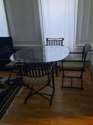 Un área de comedor con una mesa redonda de vidrio, dos sillas con asientos acolchados y un tapete estampado sobre el piso de madera.