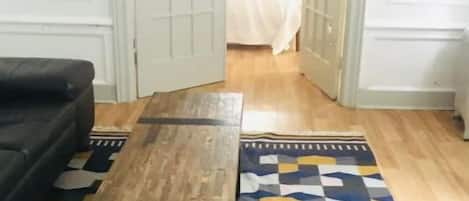 A room with a sofa, a wooden bench, and a patterned rug on a wooden floor.