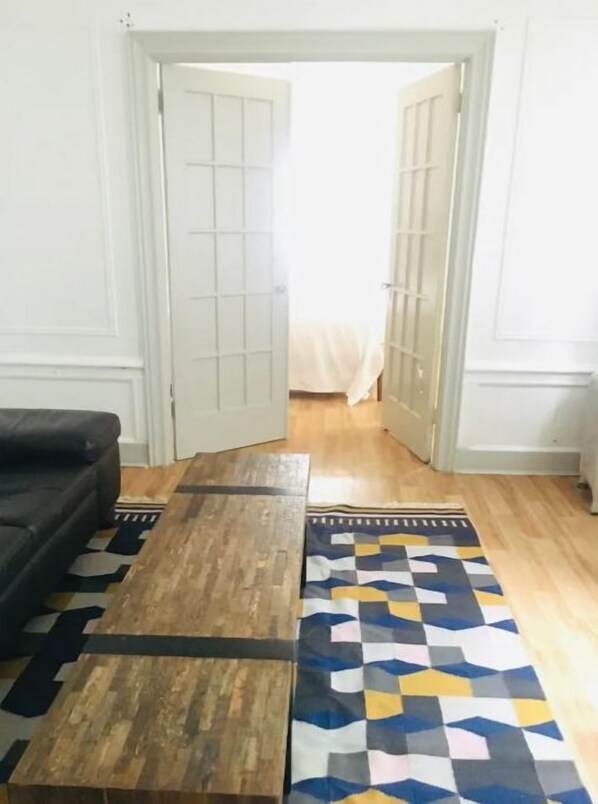 Una habitación con un sofá, un banco de madera y una alfombra estampada sobre piso de madera.