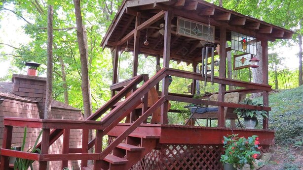 Une terrasse en bois avec un escalier menant à un espace abrité doté d’une fenêtre et d’un luminaire suspendu.