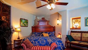 Une chambre avec un lit en bois, un ventilateur de plafond, un tableau et une lampe.