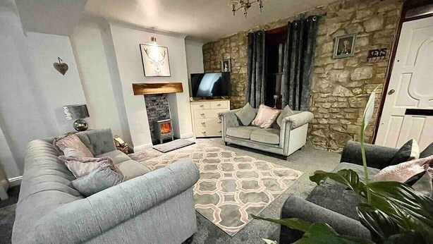 A living room with a sofa set, a stone wall, a fireplace, and a television. - A Superb Size Cottage By The Canal (Torfaen)
