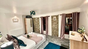 A bedroom with a bed, a desk, a chair, a radiator, a window with curtains, and a stone wall. - A Superb Size Cottage By The Canal (Torfaen)