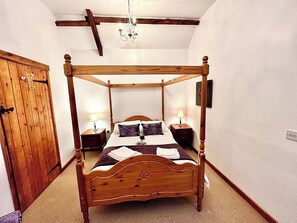 A four-poster bed with a wooden headboard, two bedside tables, a nightstand, and a chandelier. - 4 beautiful stone barns SlEEPS 17 People (Monmouthshire)