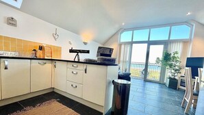 A modern kitchen with white cabinets, a black countertop, and a large window offering a view of the outdoors. - Sea Views, Hot tub, Balcony, 4 star Visit Wales (Pendine Camartheshire)
