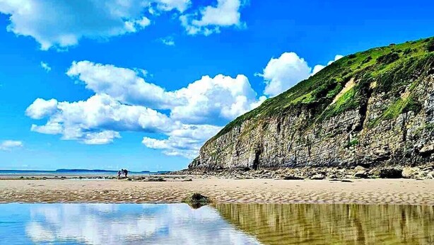 A beach with clear water reflecting the sky and clouds, a rocky cliff with greenery, and a distant view of the sea. - Sea Views, Hot tub, Balcony, 4 star Visit Wales (Pendine Camartheshire)