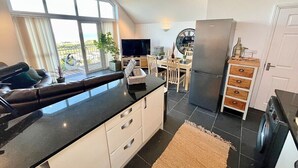 A modern kitchen with a large island, a dining area with a table and chairs, and a view of the outdoors through large windows. - Sea Views, Hot tub, Balcony, 4 star Visit Wales (Pendine Camartheshire)