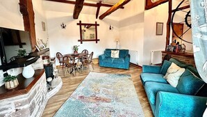 Ein gemütliches Wohnzimmer mit einem blauen Sofa, Holzbalken, einer Chandelier und einem Essbereich mit Stühlen und einem Tisch.