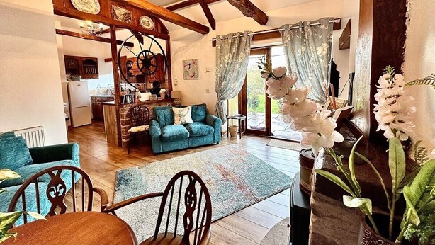 Ein gemütliches Wohnzimmer mit Holzbalkendecke, einem blauen Sofa und einem Essbereich mit Tisch und Stühlen.