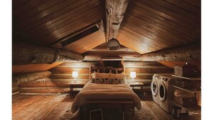 A log cabin bedroom with a bed, two bedside lamps, a washing machine, and a rustic wooden ceiling. - Cozy, Modern Log Cabin Getaway ~ 20 Min to Winter Park (Tabernash)
