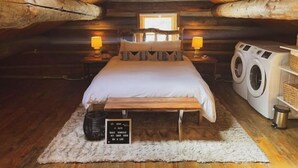 A cozy attic bedroom with a wooden bed, two bedside lamps, a washing machine, and a sign on the floor. - Cozy, Modern Log Cabin Getaway ~ 20 Min to Winter Park (Tabernash)