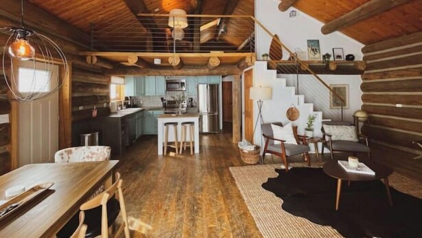 A rustic cabin interior with a wooden ceiling, a kitchen area, a dining space, and a staircase leading to an upper level. - Cozy, Modern Log Cabin Getaway ~ 20 Min to Winter Park (Tabernash)