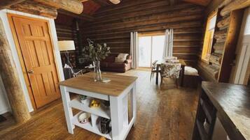 A cozy log cabin interior with a wooden dining table, a sofa, and a kitchen area.