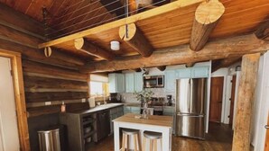 A rustic kitchen with wooden beams, a central island with stools, stainless steel appliances, and light blue cabinets. - Cozy, Modern Log Cabin Getaway ~ 20 Min to Winter Park (Tabernash)