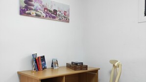 Un escritorio de madera con cajones, una silla de mimbre, un cuadro en la pared y un equipo de aire acondicionado.